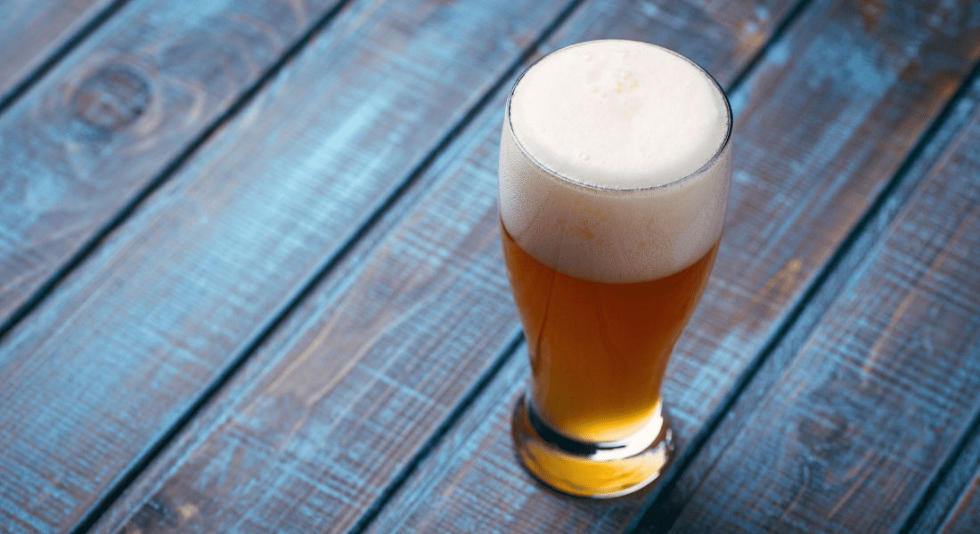 A tall glass of beer with a frothy head on a blue wooden table.